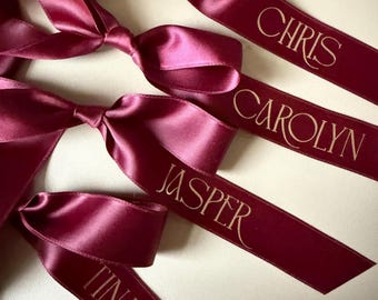 Cintas y lazos personalizados para nombres de mesa, ideales para cenas y celebraciones navideñas.