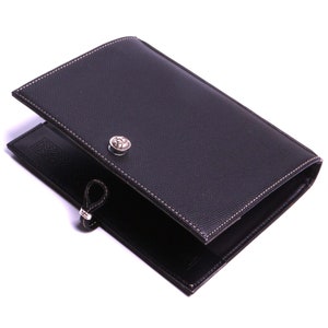 Peut inclure: Porte-passeport en cuir noir avec une fermeture à bouton argenté et une boucle argentée. Le porte-passeport a une bordure cousue et une surface texturée subtile.