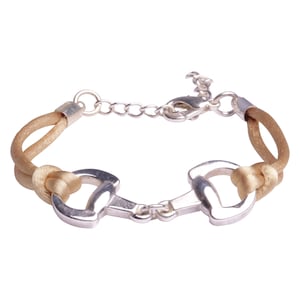 Puede incluir: Un brazalete plateado de inspiración ecuestre con una cadena y un cordón de cuero marrón.