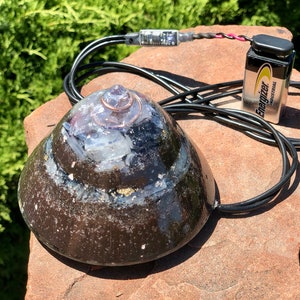 May include: A black ceramic bowl with a copper rim and a white crystal inside. The bowl is connected to a black wire and a battery pack labeled "Energizer Industrial".