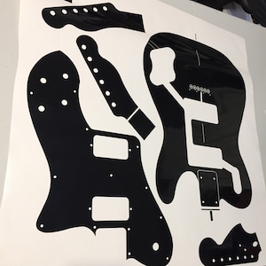May include: Black and white guitar template for a custom guitar build. The template includes the body, neck, and headstock.