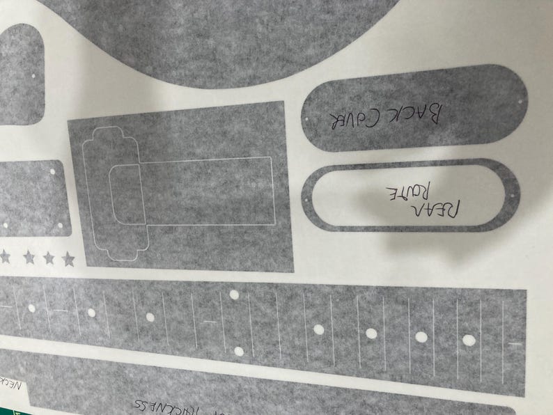 Puede incluir: Una hoja gris con varias plantillas impresas para piezas de guitarra, incluyendo un diapas&oacute;n con marcadores de puntos blancos, una secci&oacute;n de cuerpo rectangular y formas ovaladas etiquetadas "BACK COVER" y "REAR ROUTE" en tinta negra, con cuatro estrellas peque&ntilde;as.