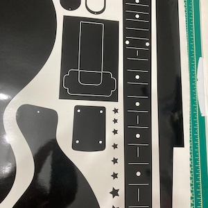 Puede incluir: Una hoja de pegatinas de vinilo negro con varias formas relacionadas con la guitarra, incluyendo un diapas&oacute;n con incrustaciones de puntos blancos, un golpeador, una placa de puente, un contorno de clavijero y estrellas.