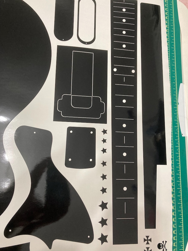 Puede incluir: Una hoja de pegatinas de vinilo negro con varias formas relacionadas con la guitarra, incluyendo un diapas&oacute;n con incrustaciones de puntos blancos, un golpeador, una placa de puente, un contorno de clavijero y estrellas.
