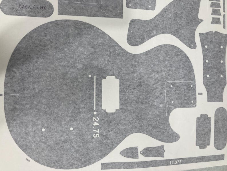 Puede incluir: Una hoja de plantilla gris con varias piezas de guitarra, incluyendo el contorno de un cuerpo de guitarra con una marca de escala de 62,865 cm, un clavijero, cavidades para pastillas y una tapa trasera sobre un fondo gris texturizado.
