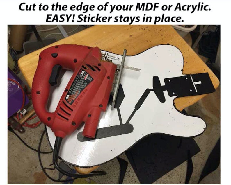 May include: A red electric jigsaw tool with a black cord is being used to cut a white guitar shape with a black sticker on it. The text "Cut to the edge of your MDF or Acrylic. EASY! Sticker stays in place." is visible at the top of the image.