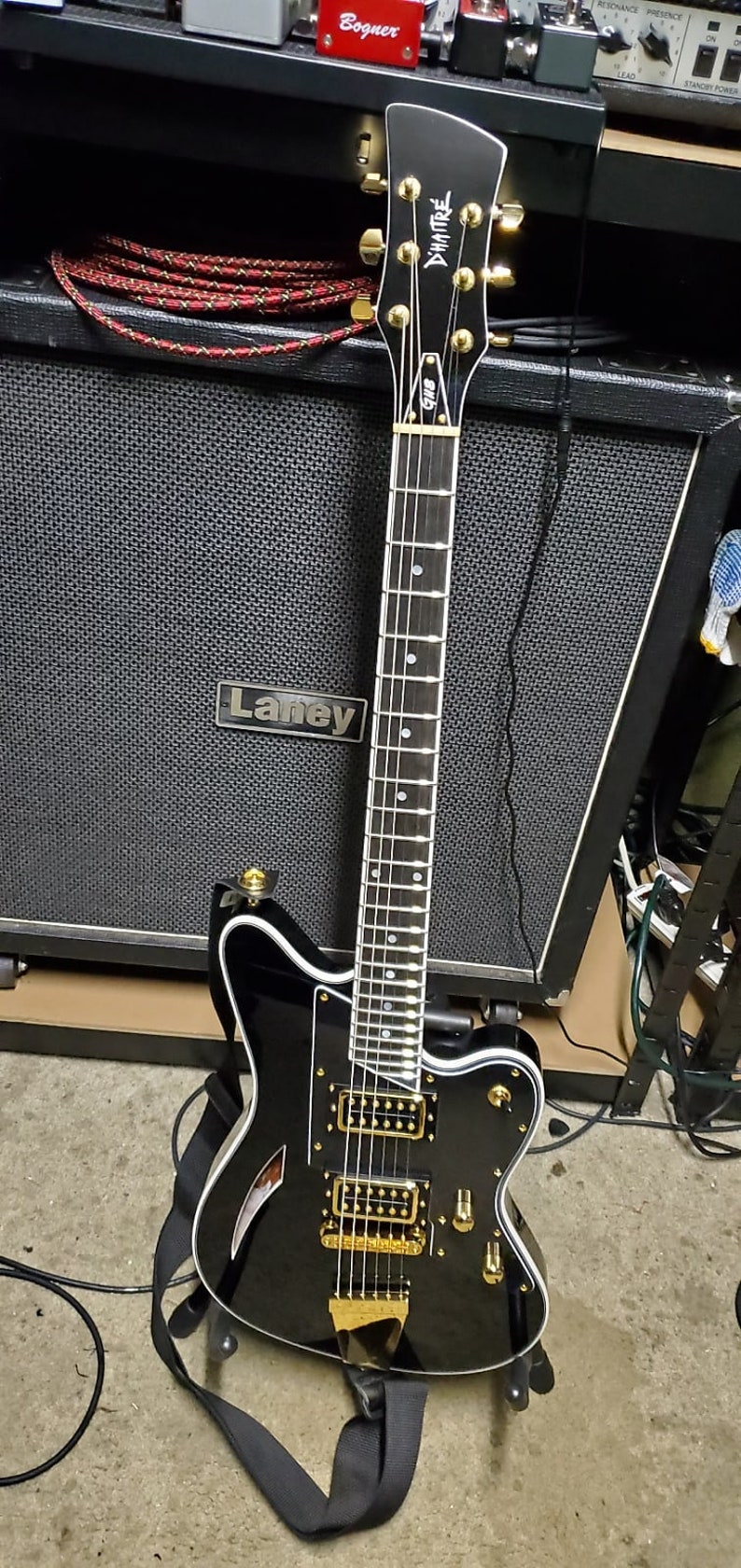 customer build surfcaster Black electric guitar with gold hardware and a white pickguard. The guitar is leaning against a black amplifier with a 'Laney' logo.