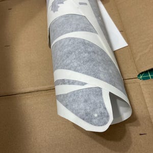 Puede incluir: Un rollo de papel de transferencia de vinilo adhesivo blanco con formas troqueladas, incluido un dise&ntilde;o de hoja de arce. La cinta de transferencia semitransparente envuelve las calcoman&iacute;as de vinilo, parcialmente despegadas del papel.