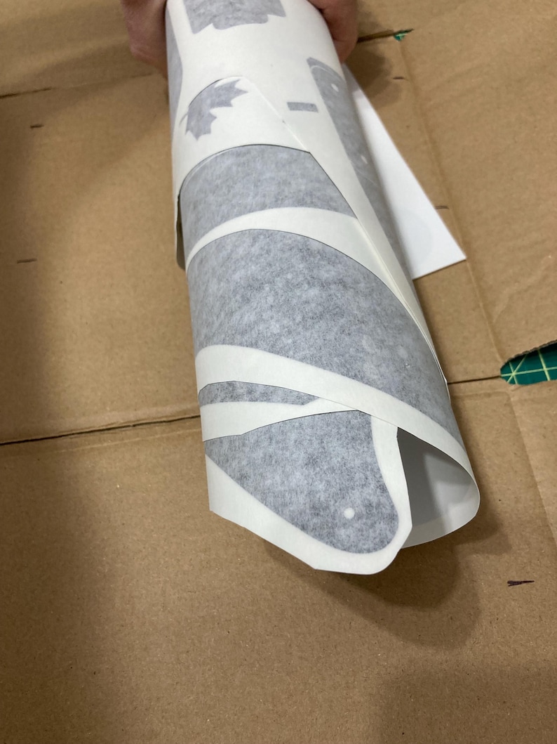 Puede incluir: Un rollo de papel de transferencia de vinilo adhesivo blanco con formas troqueladas, incluido un dise&ntilde;o de hoja de arce. La cinta de transferencia semitransparente envuelve las calcoman&iacute;as de vinilo, parcialmente despegadas del papel.