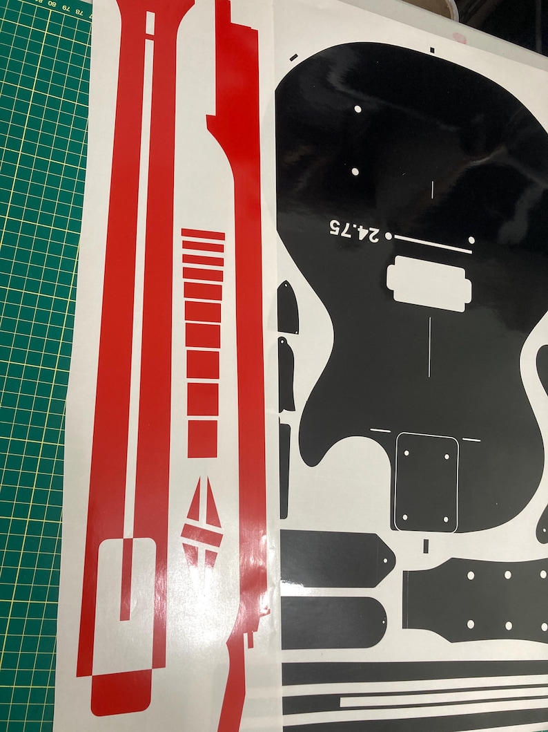 Puede incluir: Un conjunto de calcoman&iacute;as de vinilo adhesivo que incluye una tira roja larga con formas geom&eacute;tricas y una hoja negra con la silueta del cuerpo de una guitarra el&eacute;ctrica, un clavijero y varios componentes con el texto 24.75 impreso.
