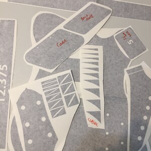 May include: A set of grey guitar body templates for a classic guitar. The templates are labelled with the words "Back Route", "Cava", "Classic", and "5-Way Switch".