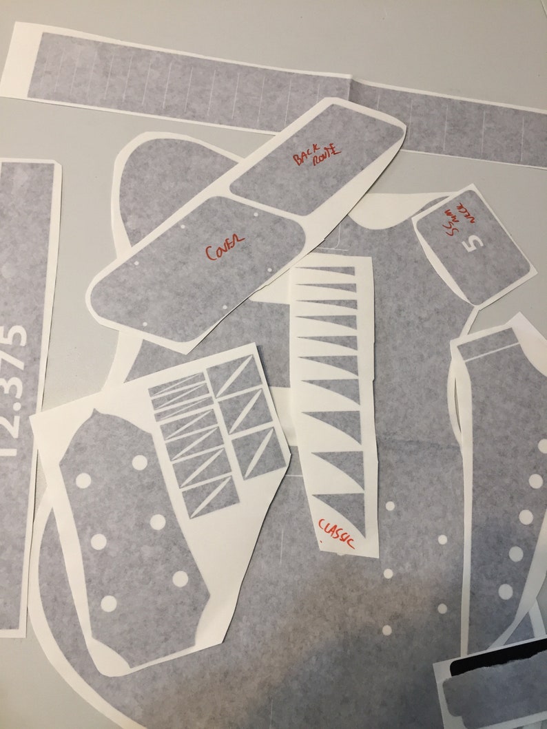 May include: A set of grey guitar body templates for a classic guitar. The templates are labelled with the words "Back Route", "Cava", "Classic", and "5-Way Switch".