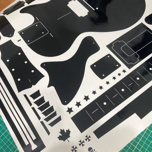 Puede incluir: Una hoja de pegatinas de vinilo negro con varias siluetas en forma de guitarra, incluyendo cuerpo, clavijero y componentes del m&aacute;stil. El dise&ntilde;o incluye elementos decorativos como estrellas, una hoja de arce e iconos de calaveras, con el texto 24.75.