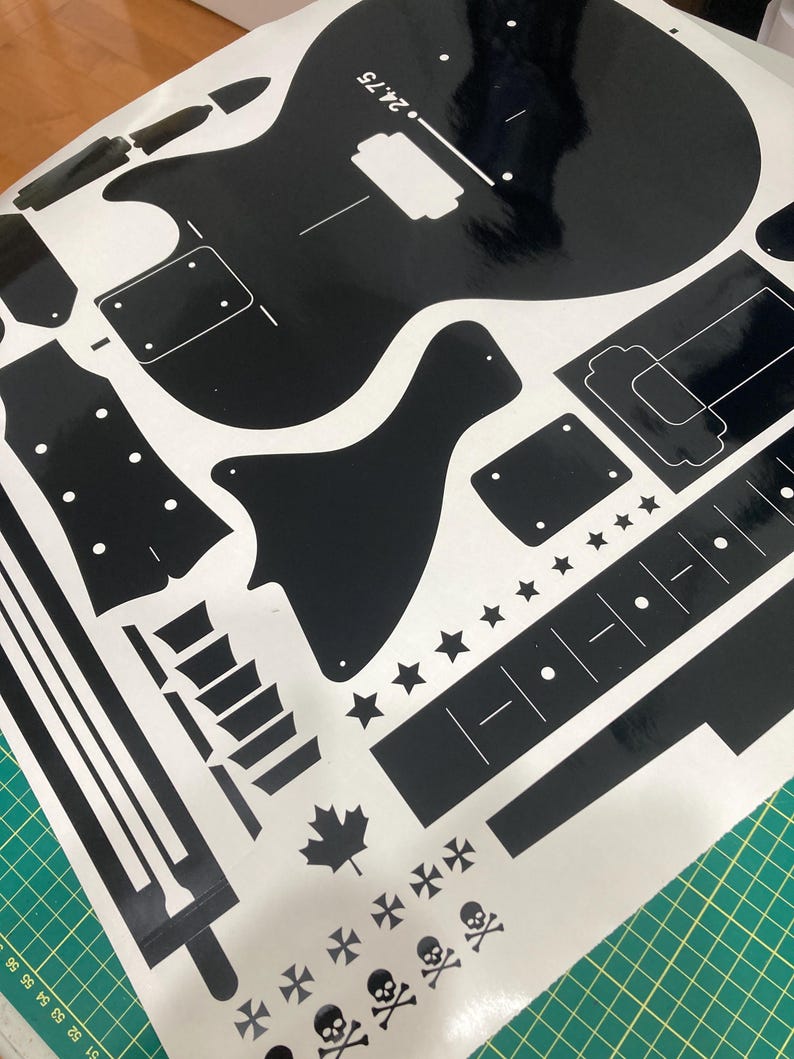 Puede incluir: Una hoja de pegatinas de vinilo negro con varias siluetas en forma de guitarra, incluyendo cuerpo, clavijero y componentes del m&aacute;stil. El dise&ntilde;o incluye elementos decorativos como estrellas, una hoja de arce e iconos de calaveras, con el texto 24.75.