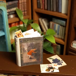 Il libro illustrato in miniatura di casa delle bambole in scala 1:12 del giardino segreto. Sono inclusi anche un segnalibro sciolto e delle cartoline.