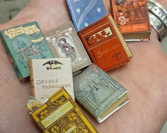 May include: A collection of miniature books with colorful covers. The titles include "The One I Knew the Best", "An Old Fashioned Girl", "Jane Eyre", "Rose Book", "Shelley", "Little Women", and "George Washington".