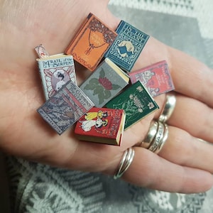 May include: A collection of miniature vintage books with colourful covers and titles such as "The Trail of the Serpent", "The Clown's Protect", "In the Levant", and "Flora's Harp".