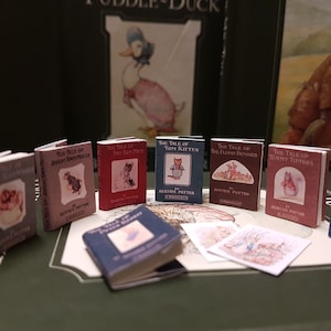 Peut inclure: Une collection de livres miniatures de Beatrix Potter mettant en scène divers personnages comme Peter Rabbit, Tom Kitten et Timmy Tiptoes. Les livres sont disposés sur une surface brune avec un livre plus grand en arrière-plan.