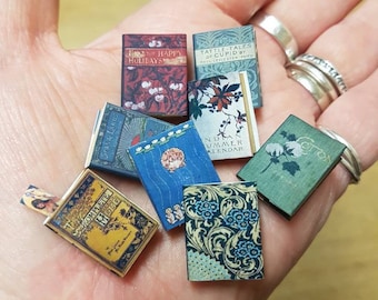 May include: A collection of miniature books with various colorful covers and titles, including "The Happy Holidays", "Tattle-Tales of Cupid", "Indian Summer Calendar", and "Cotton".
