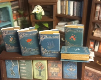 May include: Miniature books with blue covers and gold lettering, featuring floral illustrations. The books are labeled "FAMILIARS" and "WILDFLOWERS". They are arranged on a small wooden shelf, with other miniature books below.