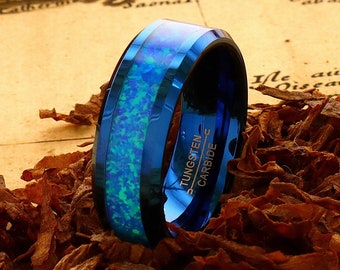 May include: A blue and silver tungsten carbide ring with an opal inlay. The ring is sitting on a pile of brown tobacco.