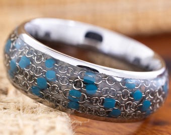 May include: A silver ring with a unique design. The ring features a chainmail pattern filled with small, bright blue accents. The band is polished and smooth, creating a striking contrast with the textured interior. This ring is a stylish accessory.