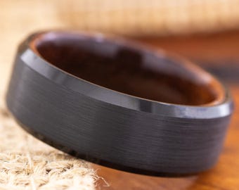 May include: A black ring with a brushed metal finish and a dark wood interior. The ring is set against a neutral background, highlighting its modern design. The ring's width is approximately 8mm.