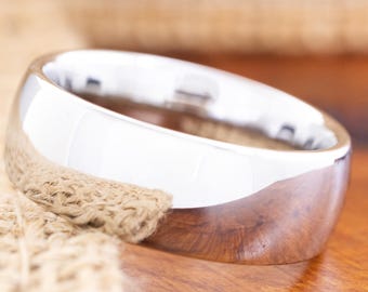 May include: A polished, silver-colored ring with a rounded band. The ring reflects the light, creating a bright, shiny appearance. The ring is set against a neutral background, highlighting its simple elegance. A classic piece of jewelry.