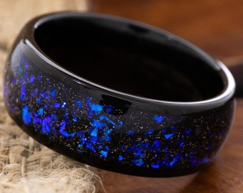 May include: A black ring with blue glitter embedded in the resin. The ring is a wide band with a smooth, polished finish.