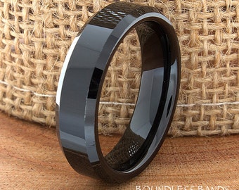 May include: A polished black ring with a beveled edge design. The ring features a smooth, reflective surface and is positioned upright. The text "BOUNDLESS BANDS" is printed in white on the surface below the ring.