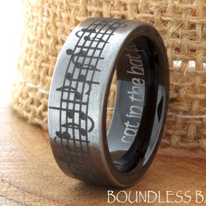 May include: A black and silver ring with a musical note design. The inside of the ring is engraved with the text "Not in the boat to"