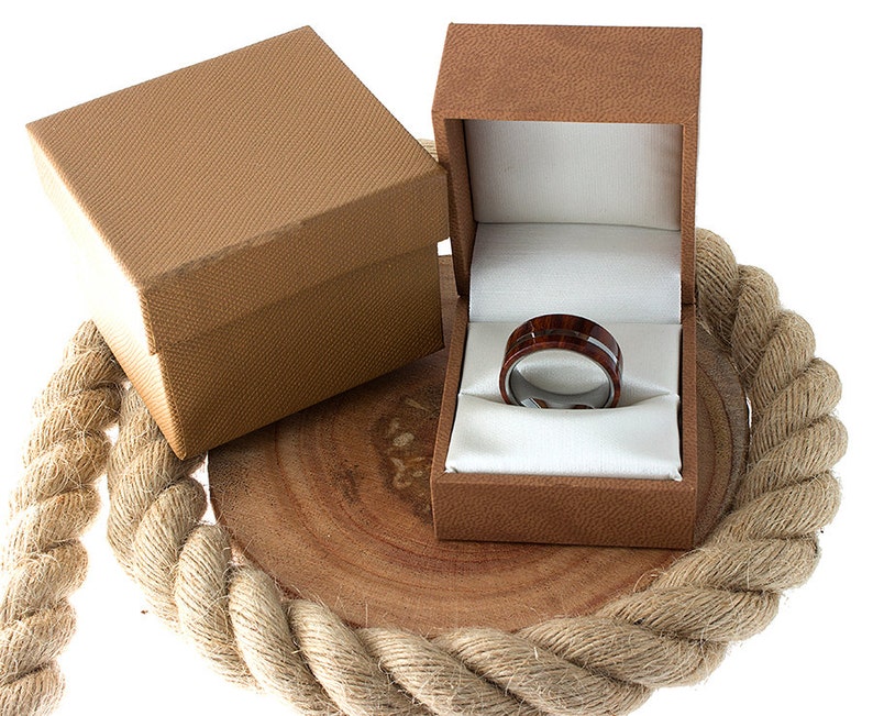 May include: A brown wooden ring box with a white satin interior. A dark brown and silver ring with a wood inlay is displayed inside the box.