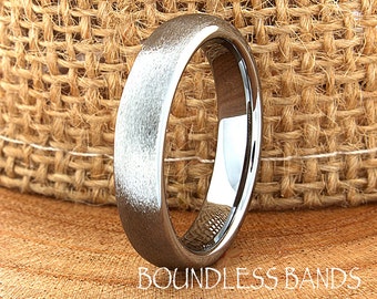 May include: A brushed silver tungsten carbide wedding band. The band has a matte finish and a rounded edge.