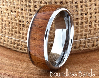 May include: A silver and brown tungsten carbide ring with a wood inlay. The ring is on a burlap background.