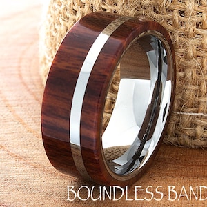 Op de afbeelding: Een ring met een gepolijste donkerbruine houtnerf buitenkant met een gecentreerde, gladde zilverkleurige metalen inleg en een reflecterende zilverkleurige binnenband. De tekst BOUNDLESS BANDS staat onderaan in het wit gedrukt.