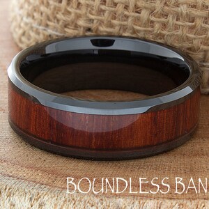 Op de afbeelding: Een zwarte keramische ring met een rode houten inlay. De ring is afgeschuind en heeft een gepolijste afwerking. Boundless Bands.