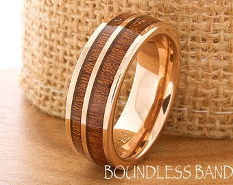 May include: A rose gold tungsten carbide ring with a brown wood inlay. The ring has two thin lines of rose gold running along the wood inlay.