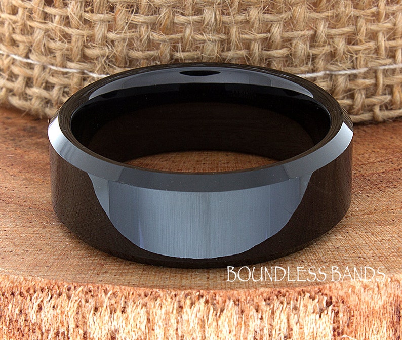 May include: A black ceramic wedding band with a beveled edge. The band has a polished finish and is made of durable tungsten carbide.
