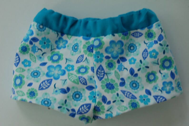May include: Blue and white floral print swim shorts with a turquoise waistband.