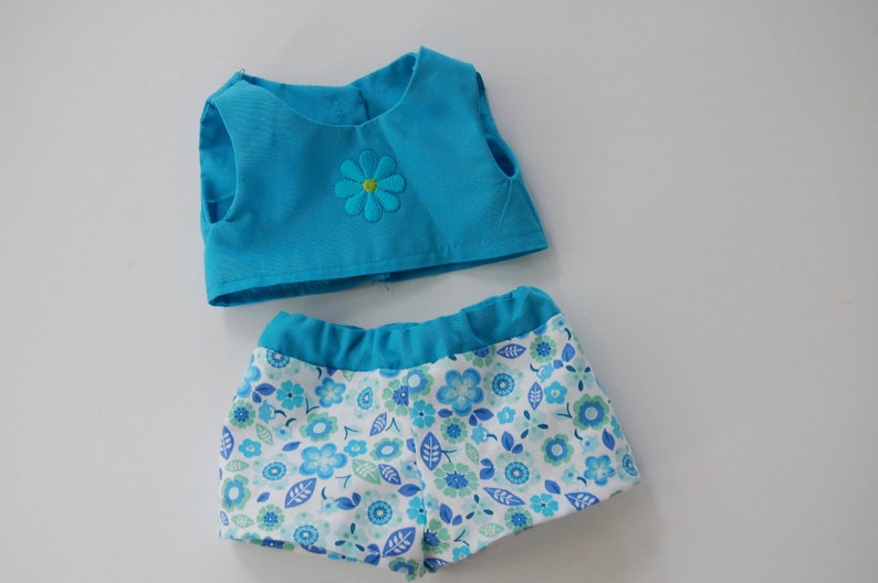 May include: A two-piece doll outfit with a sleeveless turquoise top and a white and blue floral print bottom.