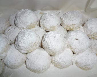 May include: A close-up of a plate of white powdered sugar cookies. The cookies are round and have a soft, fluffy texture.