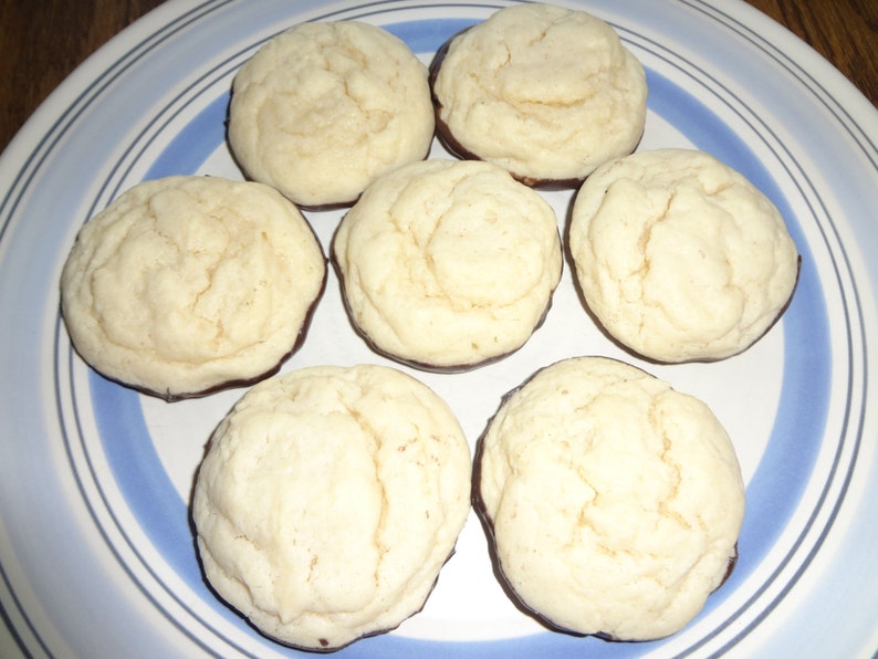 May include: A plate of six round cookies with a chocolate coating on the bottom. The cookies are light brown and have a slightly rough texture.