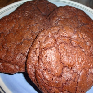 May include: Four chocolate chip cookies on a blue and white plate. The cookies are a deep brown color and have a slightly cracked surface.