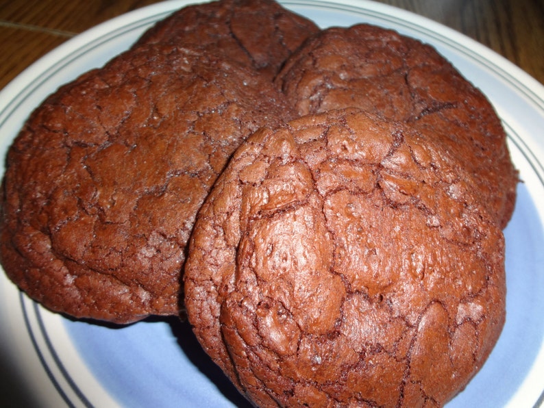 May include: Four chocolate chip cookies on a blue and white plate. The cookies are a deep brown color and have a slightly cracked surface.