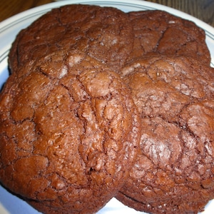 May include: Four chocolate chip cookies on a blue and white plate. The cookies are a dark brown color and have a slightly cracked surface.
