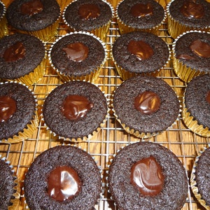 May include: A close-up of a wire rack filled with chocolate cupcakes topped with a layer of chocolate ganache.
