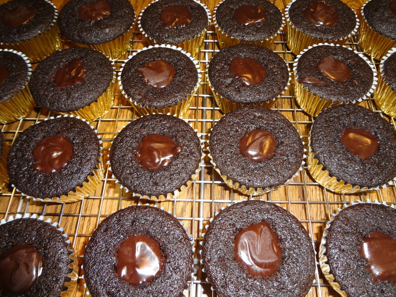 May include: A close-up of a wire rack filled with chocolate cupcakes topped with a layer of chocolate ganache.
