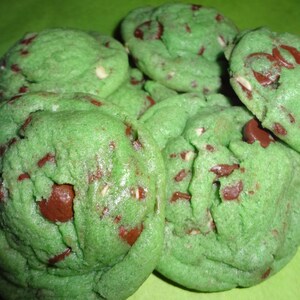 May include: A close-up of a plate of green and brown cookies with chocolate chips. The cookies are soft and chewy, and they have a minty flavor.