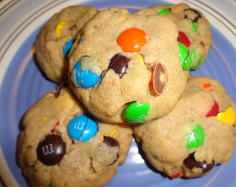May include: Close-up of four chocolate chip cookies with colorful M&M candies on a blue and white plate. The cookies are soft and chewy, with a golden brown color.