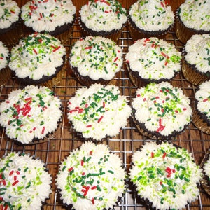 May include: A close-up of a dozen chocolate cupcakes with white icing and green and red sprinkles. The cupcakes are arranged in rows on a wire rack.